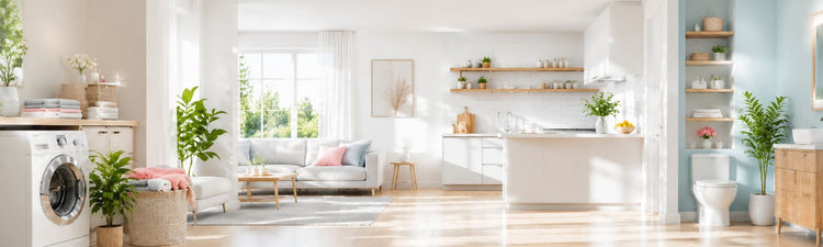 Bright modern open‑plan home interior showing laundry area, living room, kitchen, and bathroom with plants, washing machine, sofa, wooden shelves, and natural sunlight.